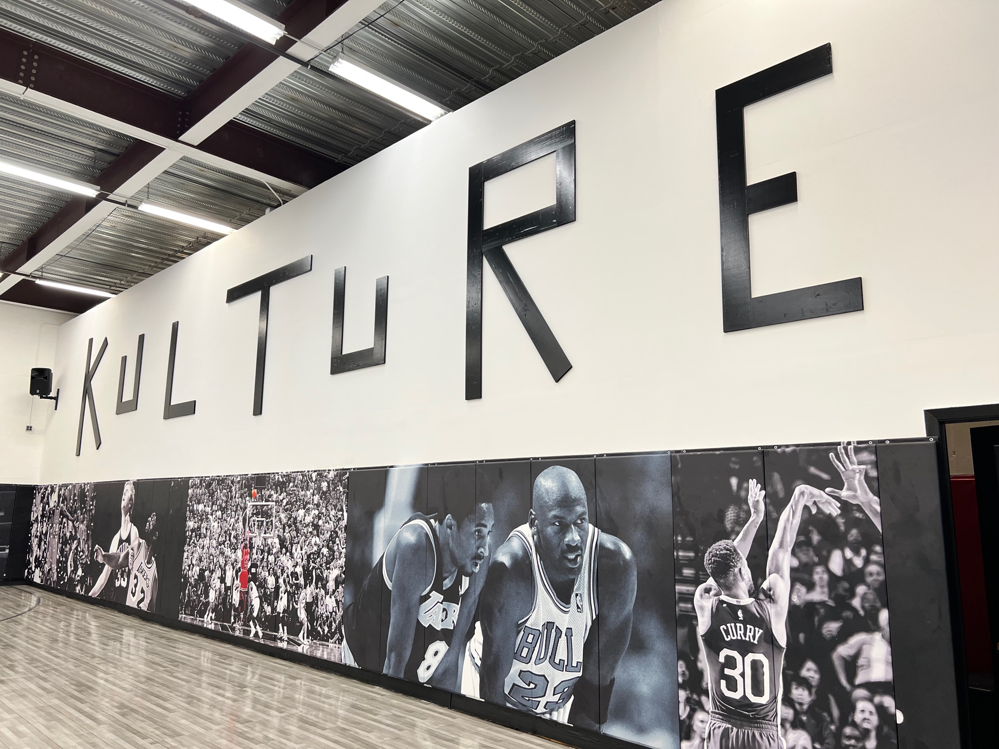 Large KULTURE sign in bold black metal lettering mounted above wall-to-wall NBA murals at the training facility