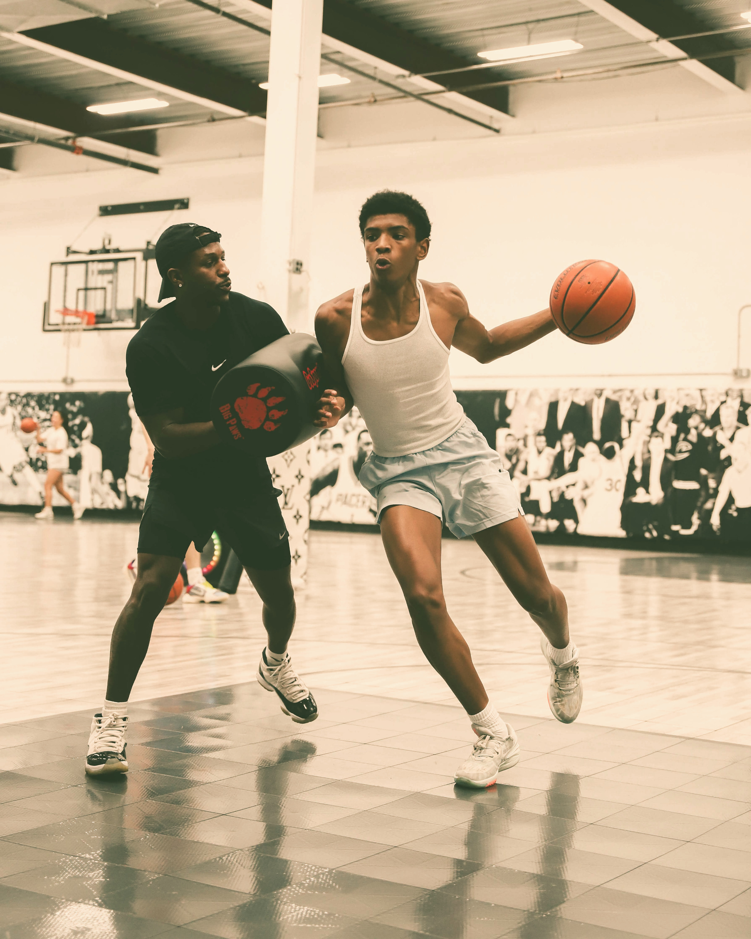 Young athlete performing an intense ball-handling drill at Kulture Basketball while a trainer applies defensive pressure with a pad